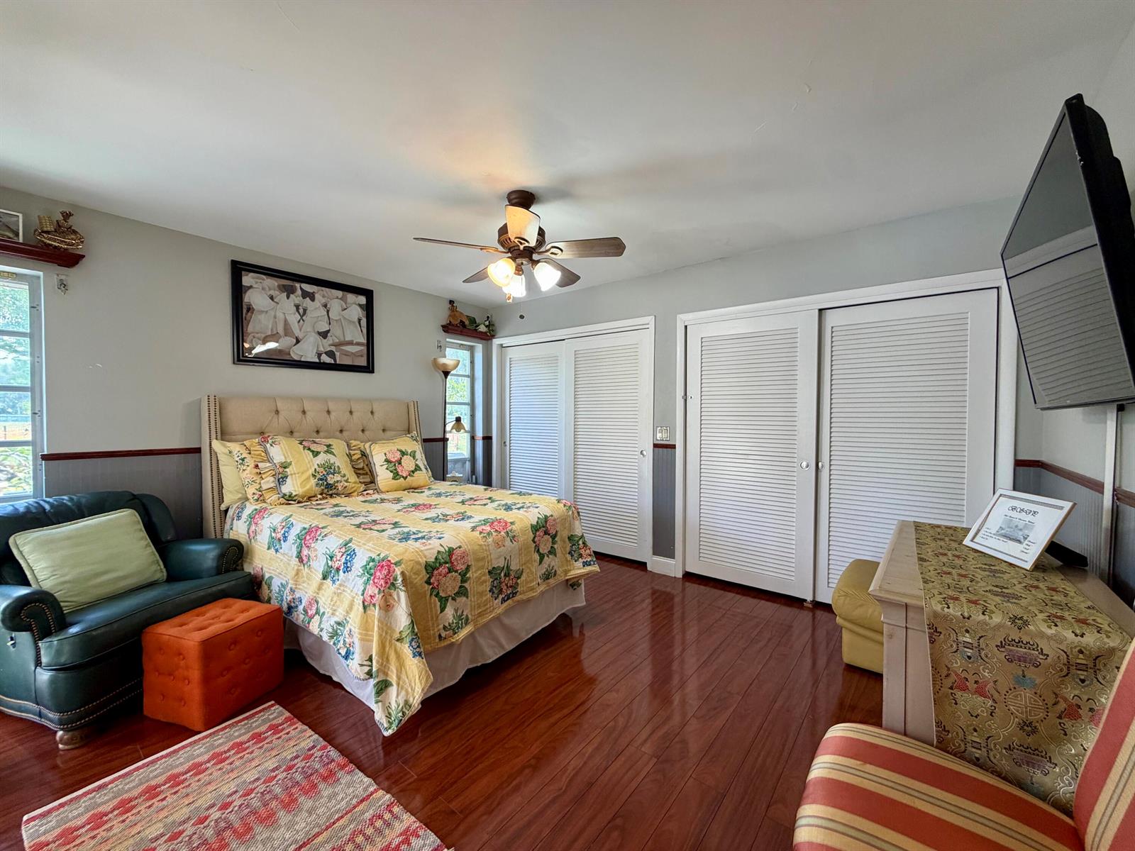 A bedroom features a floral bed, hardwood floors, white louvered closet doors, and a ceiling fan — TAMARAC, FL