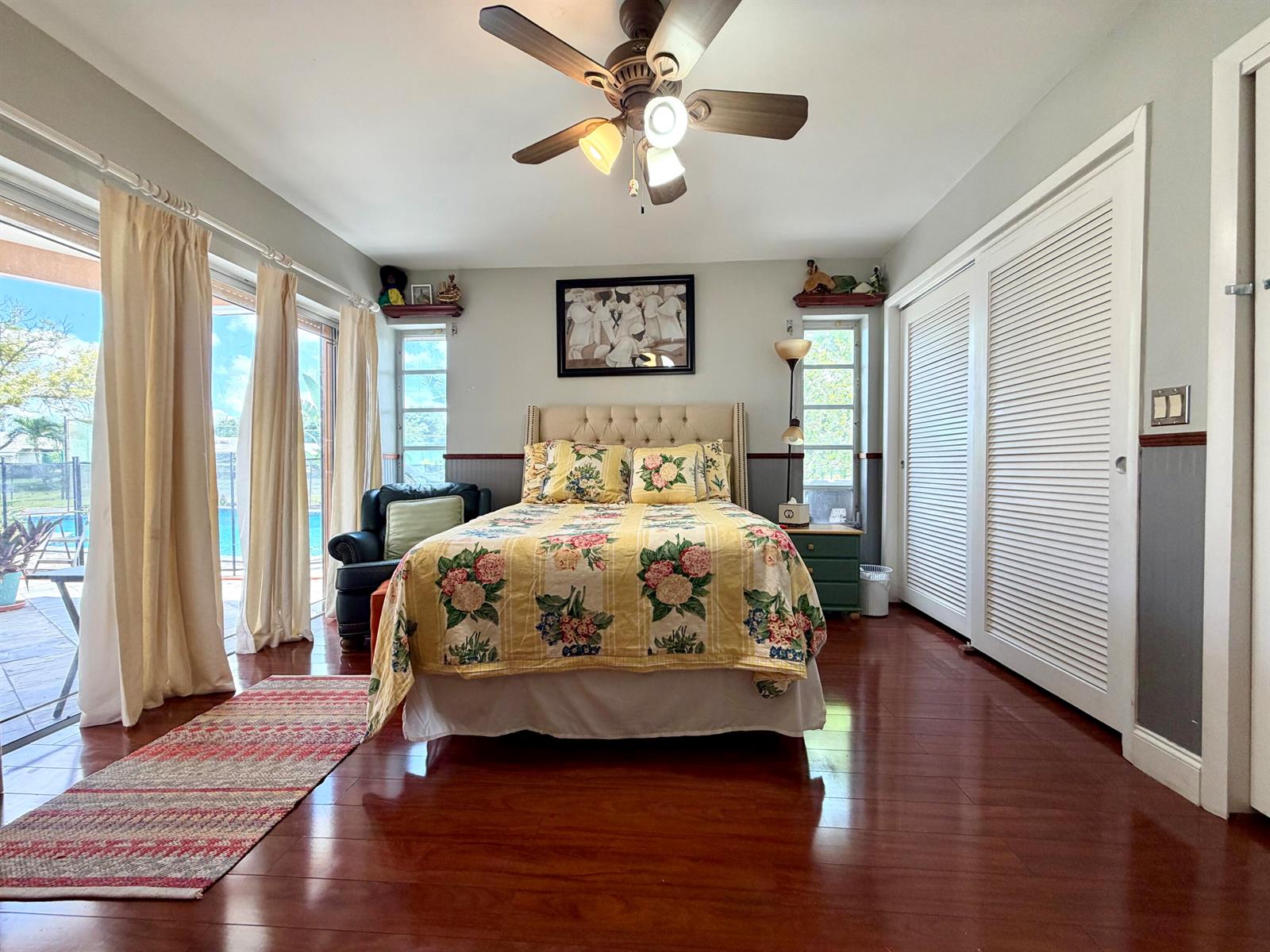 A bedroom features a floral bedspread, ceiling fan, hardwood floors, and sliding glass patio doors — TAMARAC, FL