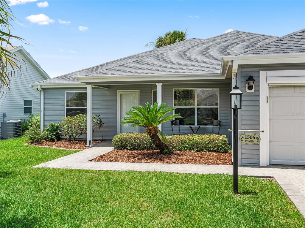 A gray house exterior features a front walkway, a small palm tree, and a garage — 1506 ROCHA LANE, THE VILLAGES, FL