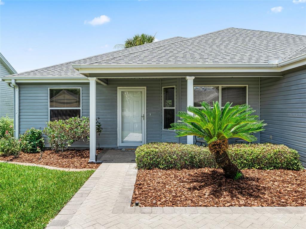 The exterior of a gray house features a paved walkway, a palm tree, and landscaping — 1506 ROCHA LANE, THE VILLAGES, FL