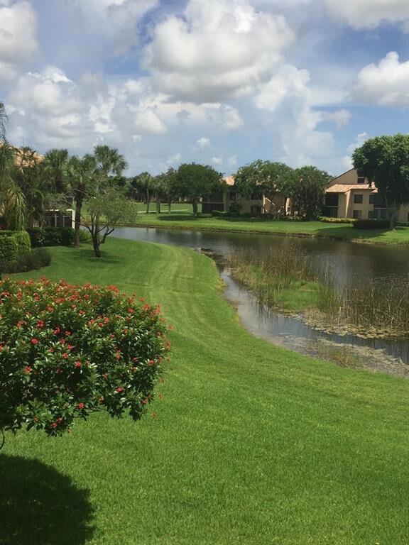 A grassy lawn slopes down to a pond with apartment buildings in the background — 7344 Clunie Place # 13604, Delray Beach FL 33446, DELRAY BEACH, FL