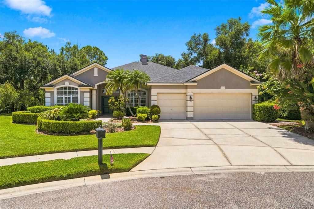 A single-story suburban house with a gray roof, tan stucco exterior, and a landscaped lawn — 6121 CHENE COURT, LUTZ, FL