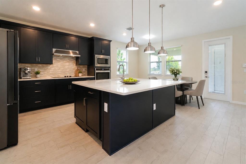 A modern kitchen features dark cabinetry, a large white quartz island, and light wood flooring — 6570 ROVER WAY, ST CLOUD, FL