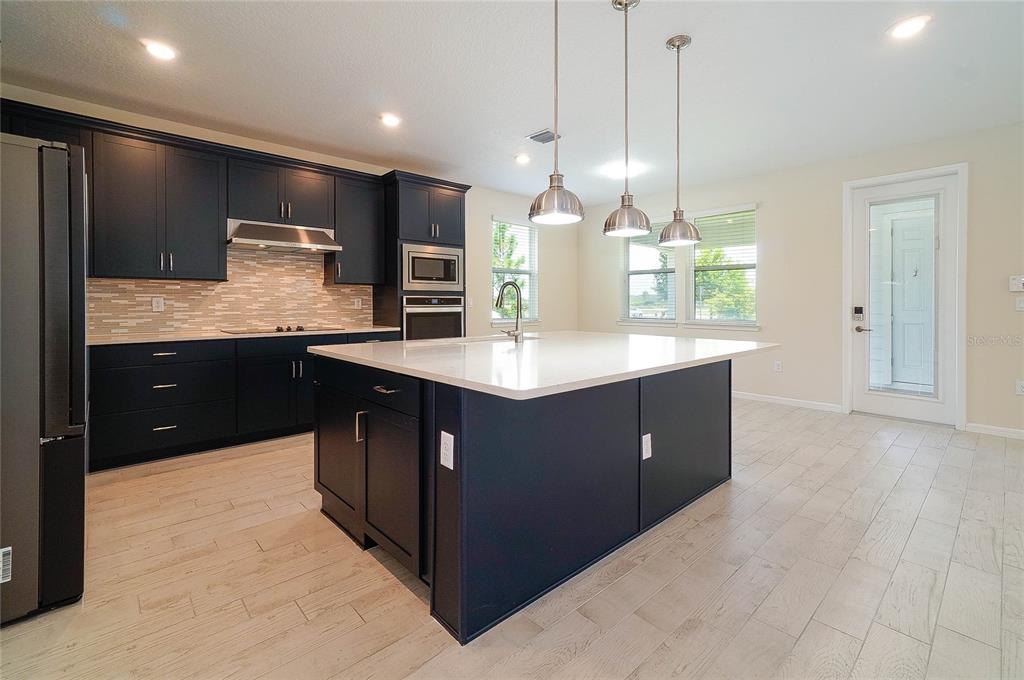 A kitchen features dark cabinets, a large white-topped island, and light wood-look flooring — 6570 ROVER WAY, ST CLOUD, FL