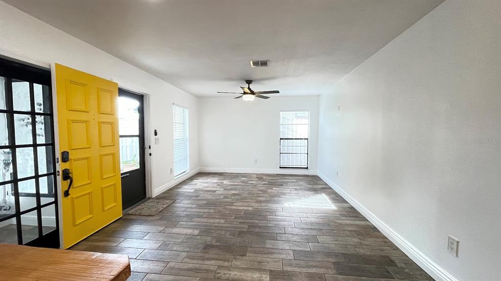 A bright living room features wood-look tile flooring, white walls, and a yellow front door — 6181 SPRINGWATER STREET, ORLANDO, FL