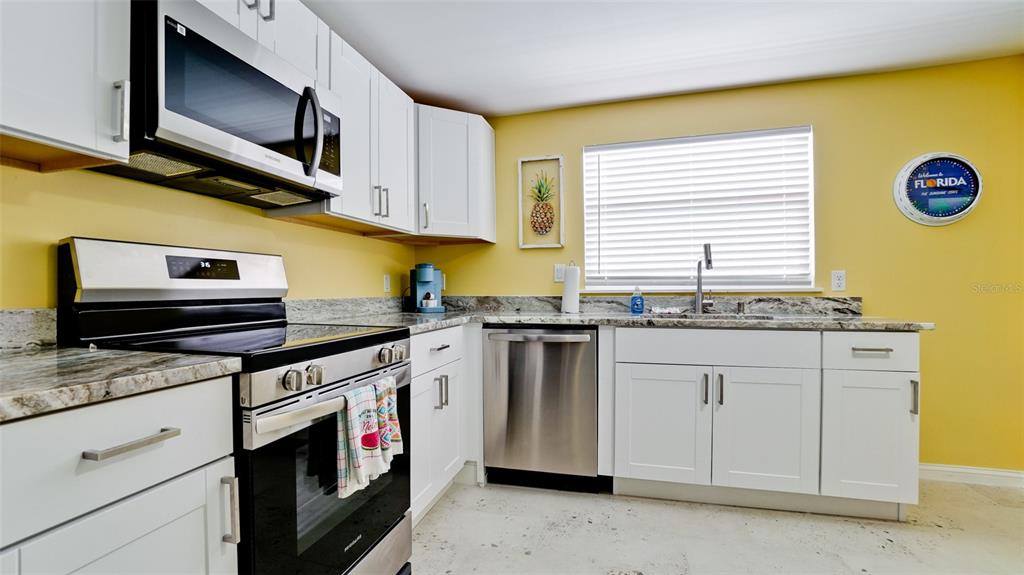 A kitchen features white cabinets, stainless steel appliances, granite countertops, and yellow walls — 601 SAINT JUDES DRIVE, LONGBOAT KEY, FL