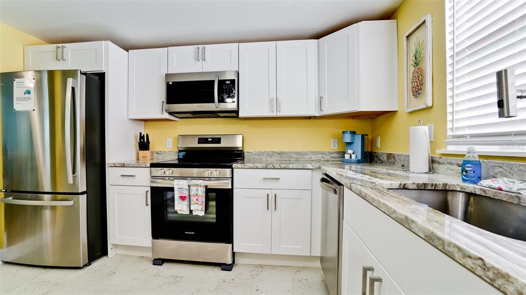 A kitchen features white cabinets, stainless steel appliances, and granite countertops against yellow walls — 601 SAINT JUDES DRIVE, LONGBOAT KEY, FL