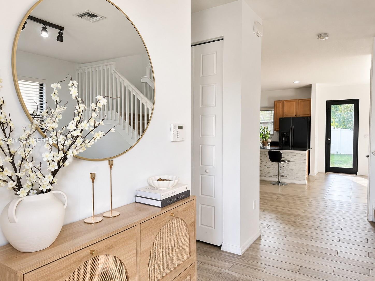 A foyer with a round mirror and wood console leads to a kitchen with bar seating — 19316 NE 8th Ct, Miami FL 33179, MIAMI, FL