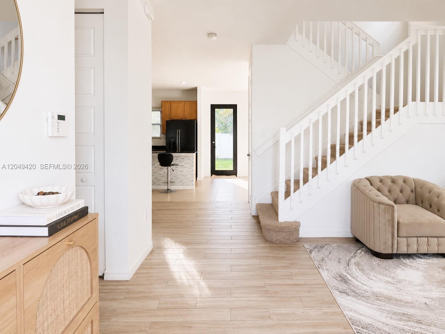 A bright entryway features light wood-look tile flooring, a staircase with white railings, and a kitchen — 19316 NE 8th Ct, Miami FL 33179, MIAMI, FL