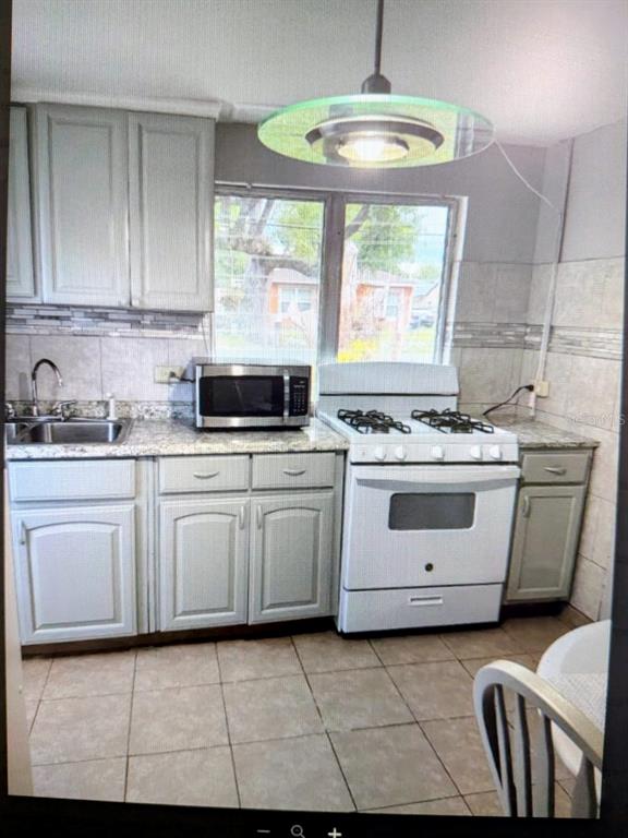 A kitchen features light gray cabinets, a white gas stove, a microwave, and tiled flooring — 2725 SAMPLE STREET, KISSIMMEE, FL