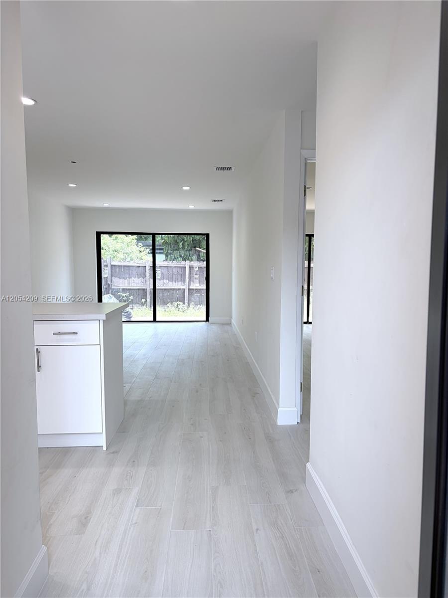 A bright, minimalist room features light-colored wood-look flooring and a sliding glass door — 3809 SW 82nd Ave # 20, Miami FL 33155, MIAMI, FL