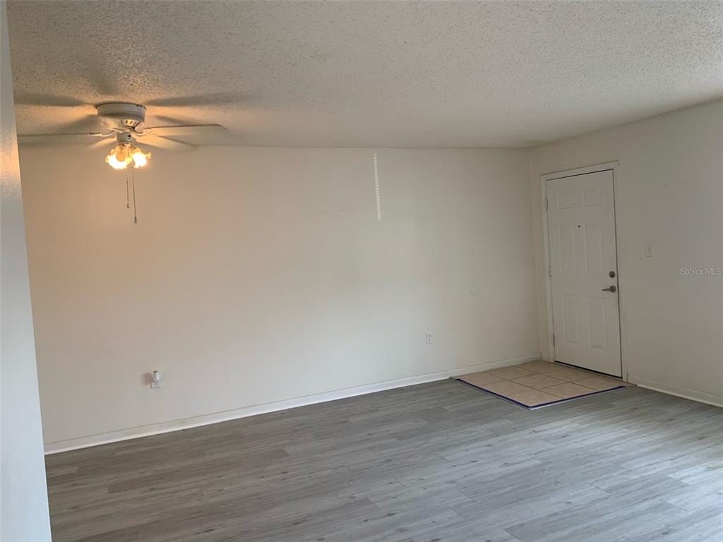 An empty living room features light gray wood-look flooring, white walls, and a ceiling fan — 12403 HIBISCUS OAK PLACE UNIT 202, TAMPA, FL