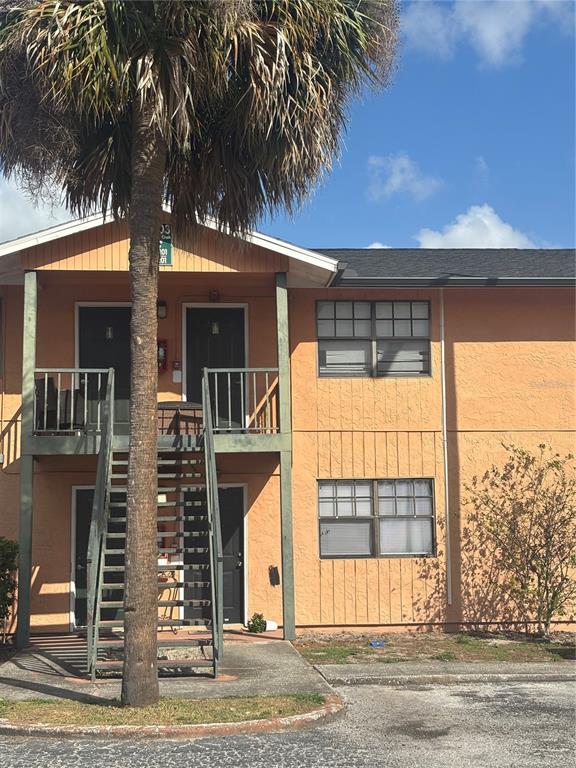 A two-story apartment building exterior features orange stucco walls, a metal staircase, and a palm tree — 12403 HIBISCUS OAK PLACE UNIT 202, TAMPA, FL