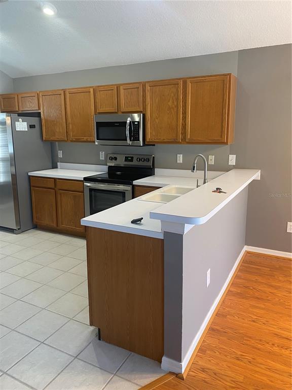 A kitchen features oak cabinets, stainless steel appliances, white countertops, and a breakfast bar — 10471 LUCAYA DRIVE, TAMPA, FL