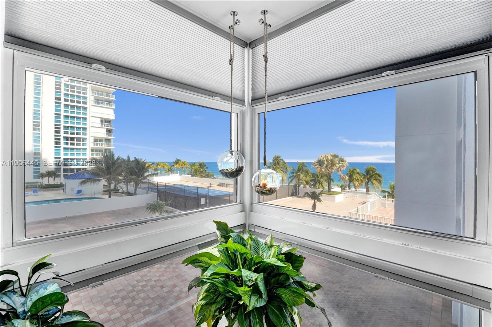 A corner room features large windows overlooking a pool, palm trees, and the ocean — 1370 S Ocean Blvd # 407, Pompano Beach FL 33062, POMPANO BEACH, FL