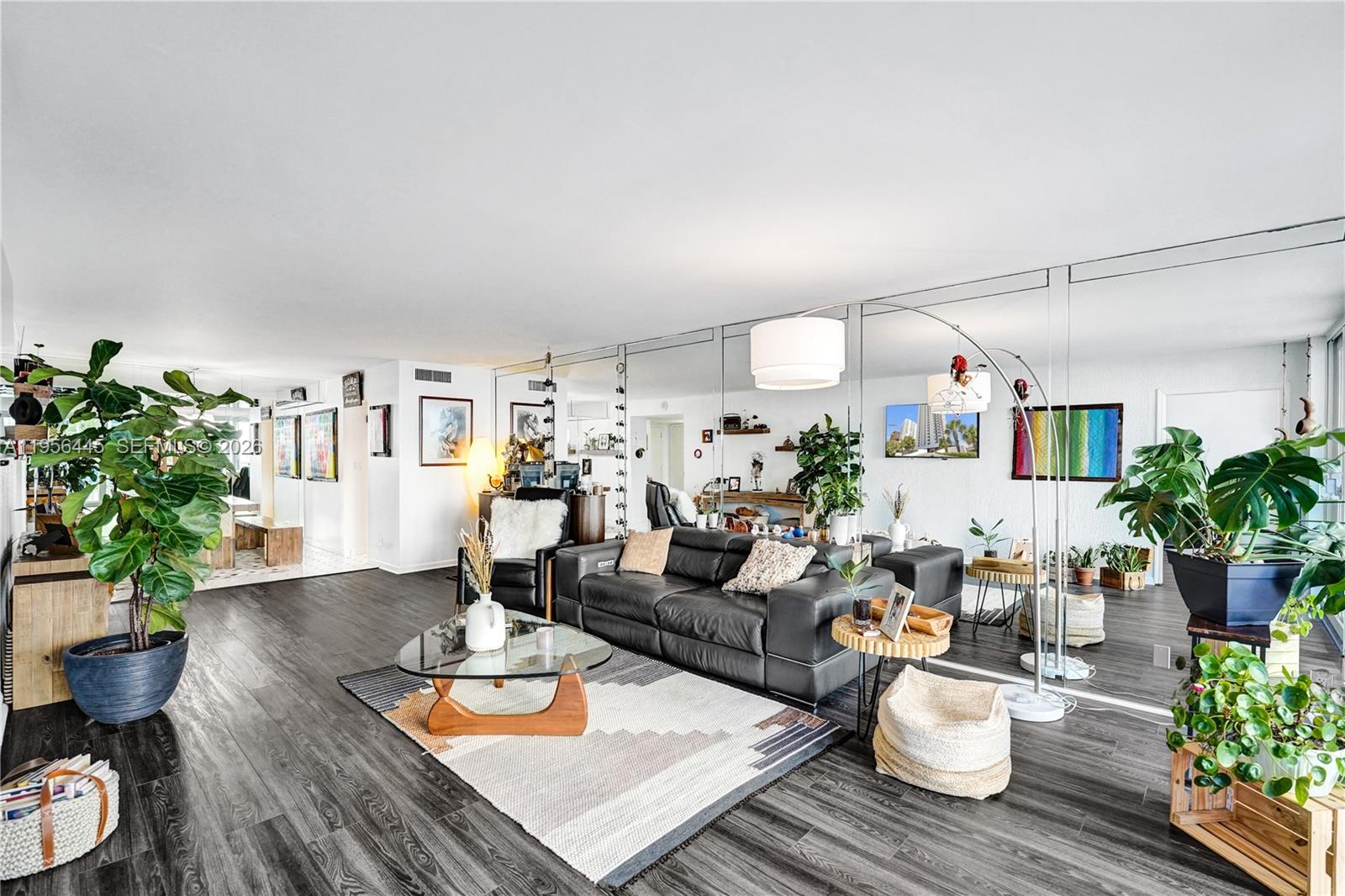 A living room features dark wood flooring, a black leather sofa, and a mirrored wall — 1370 S Ocean Blvd # 407, Pompano Beach FL 33062, POMPANO BEACH, FL