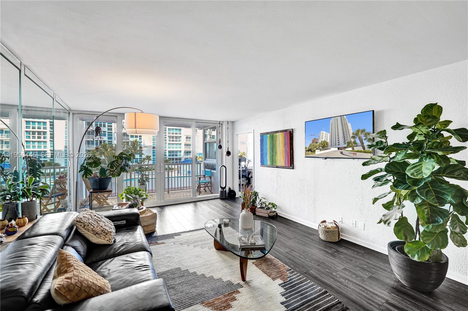 A living room features dark wood floors, a leather sofa, a glass coffee table, and plants — 1370 S Ocean Blvd # 407, Pompano Beach FL 33062, POMPANO BEACH, FL