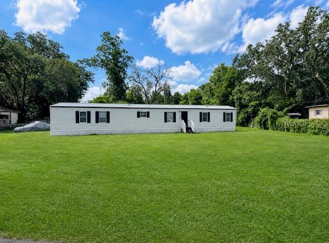 A single-story manufactured home sits on a large, grassy lot surrounded by trees — 3464 SE 91ST PLACE, OCALA, FL
