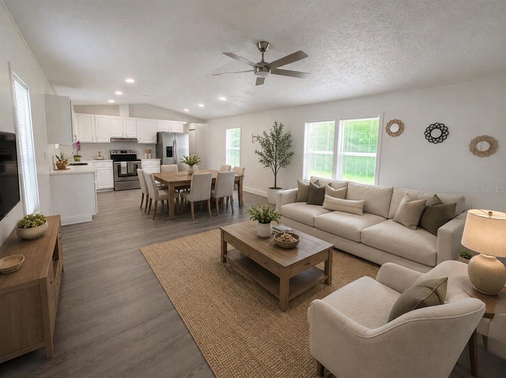 An open-concept living and dining area features white cabinetry, light wood furniture, and gray flooring — 3464 SE 91ST PLACE, OCALA, FL