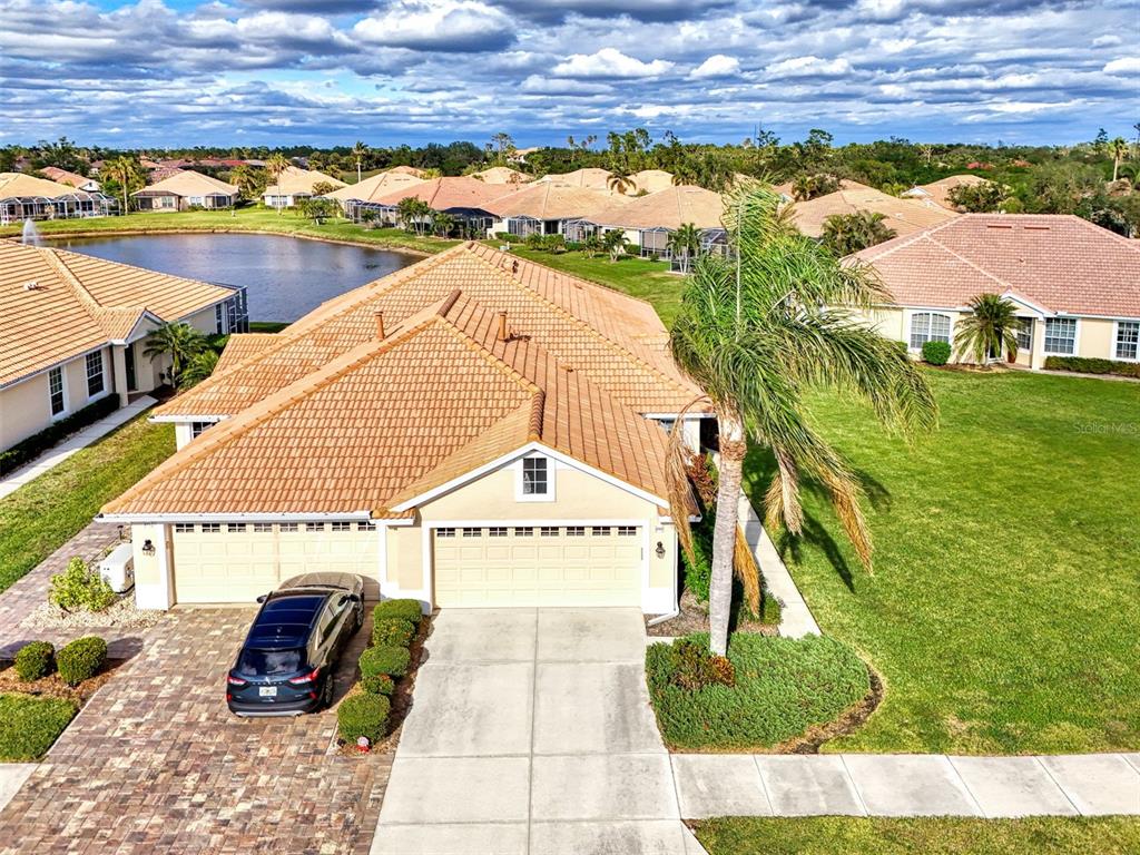 An aerial view shows a tan house with a tiled roof, a driveway, and landscaping — 4980 WHISPERING OAKS DRIVE, NORTH PORT, FL