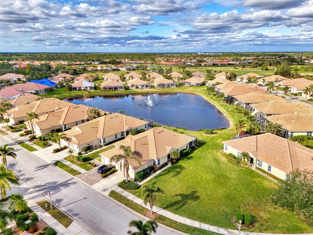 An aerial view shows a residential neighborhood with houses surrounding a central pond with fountain — 4980 WHISPERING OAKS DRIVE, NORTH PORT, FL