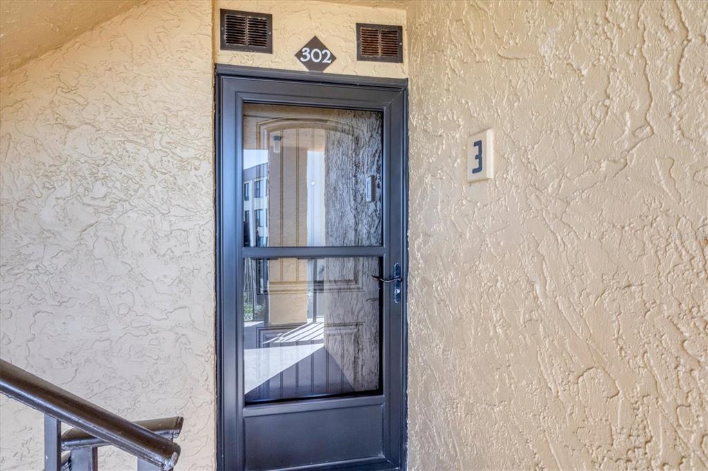 A black storm door with a glass panel is mounted on a textured beige wall — 8750 MIDNIGHT PASS ROAD UNIT 302, SARASOTA, FL