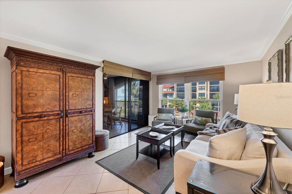 A living room features a large wooden armoire, a sofa, coffee tables, and a balcony view — 8750 MIDNIGHT PASS ROAD UNIT 302, SARASOTA, FL