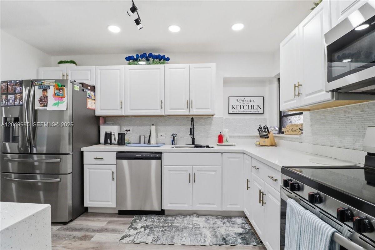 A kitchen features white cabinets, stainless steel appliances, and a light-colored tiled backsplash — 7551 Polk St, Hollywood FL 33024, HOLLYWOOD, FL