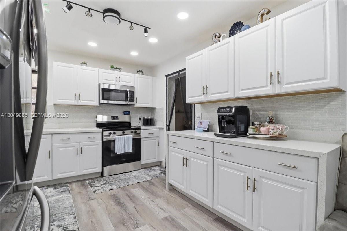 A kitchen features white cabinets, stainless steel appliances, quartz countertops, and light wood-look flooring — 7551 Polk St, Hollywood FL 33024, HOLLYWOOD, FL