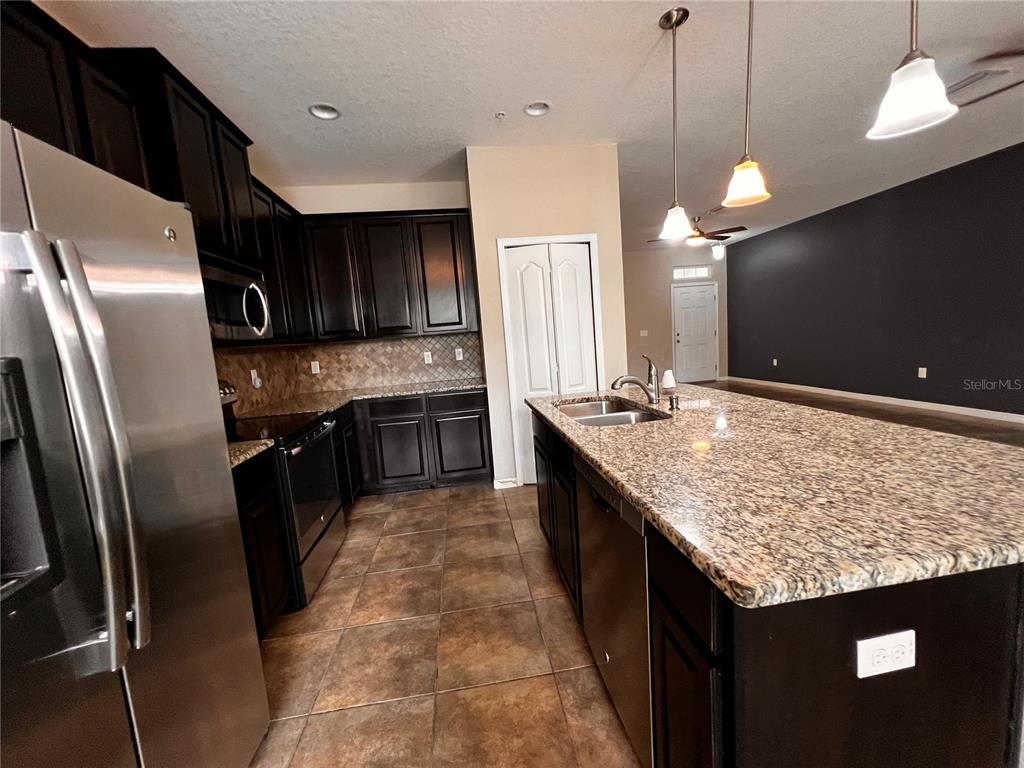 A kitchen features dark wood cabinets, granite countertops, stainless steel appliances, and tile flooring — 8613 ANDALUCIA FIELD DRIVE, TAMPA, FL