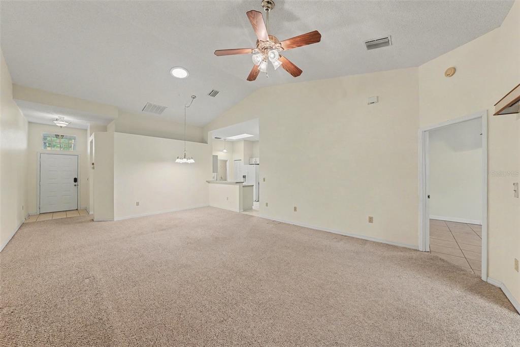 A spacious living room with beige carpet, vaulted ceilings, a ceiling fan, and an entryway — 2437 NANTUCKET HARBOR LOOP UNIT 2437, SUN CITY CENTER, FL