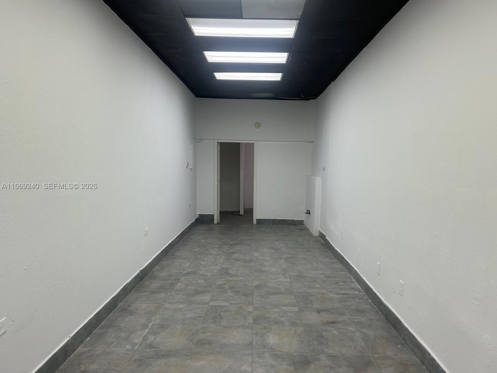 This empty commercial space features white walls, gray tiled flooring, and a black drop ceiling — 1018 71st St # 05, Miami Beach FL 33141, MIAMI BEACH, FL