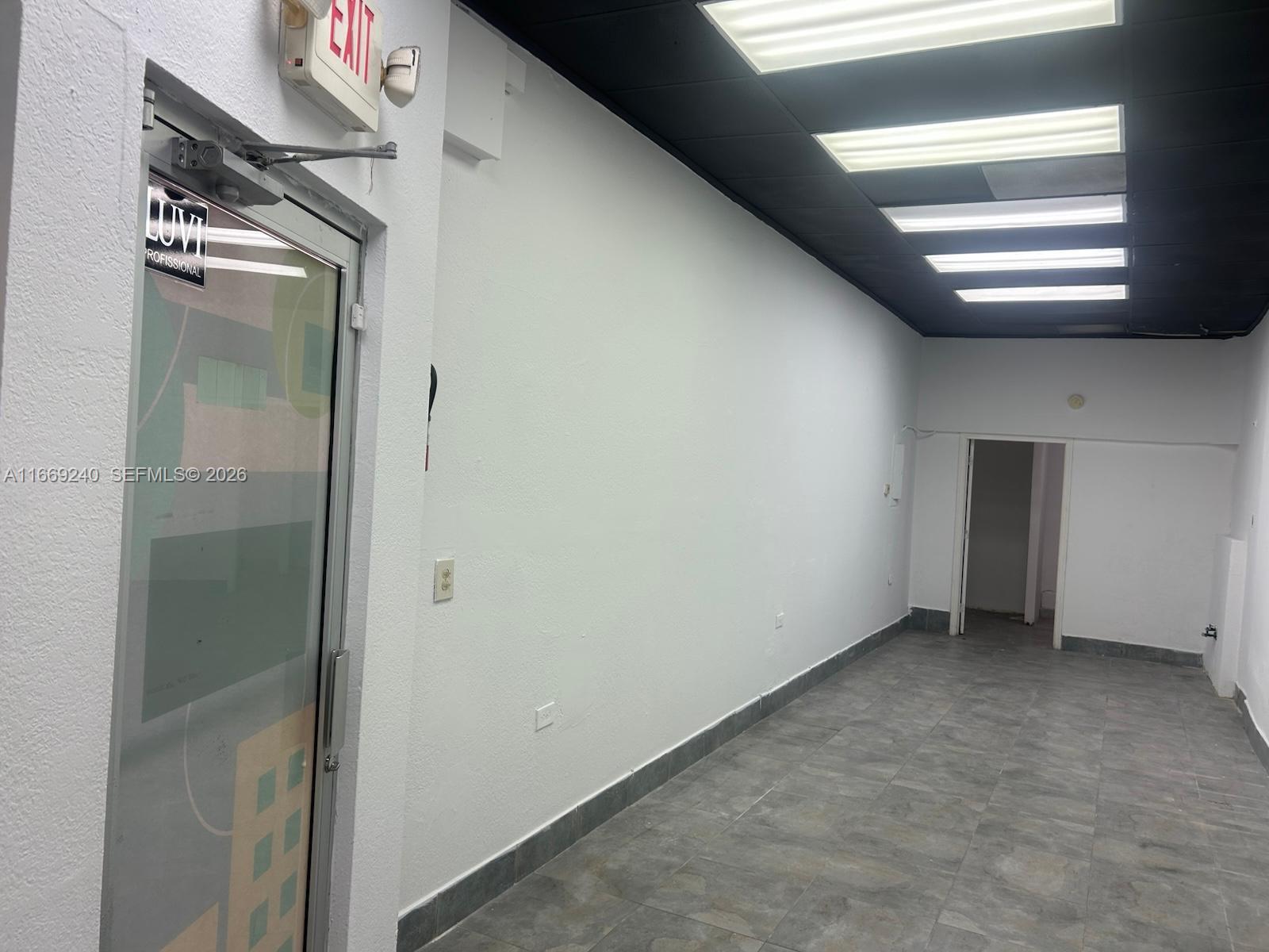 An empty commercial space with white walls, gray tiled flooring, and a black drop ceiling — 1018 71st St # 05, Miami Beach FL 33141, MIAMI BEACH, FL