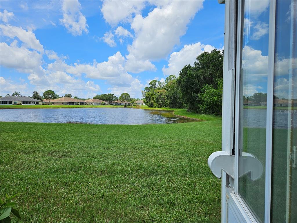 A view of a grassy backyard and a pond from a screened-in patio — 739 TREMONT GREENS LANE, SUN CITY CENTER, FL