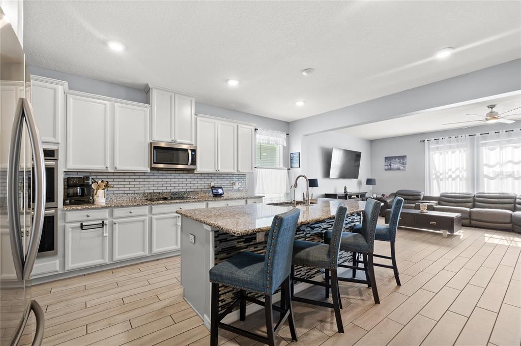 A kitchen with white cabinets, granite countertops, and a center island with blue bar stools — 12015 STONE BARK TRAIL, ORLANDO, FL