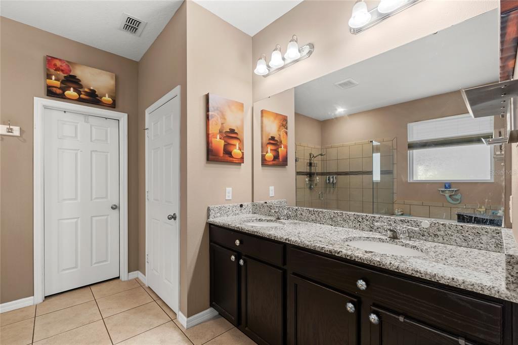 A bathroom features a double vanity with granite countertops, dark cabinets, and a large mirror — 12015 STONE BARK TRAIL, ORLANDO, FL