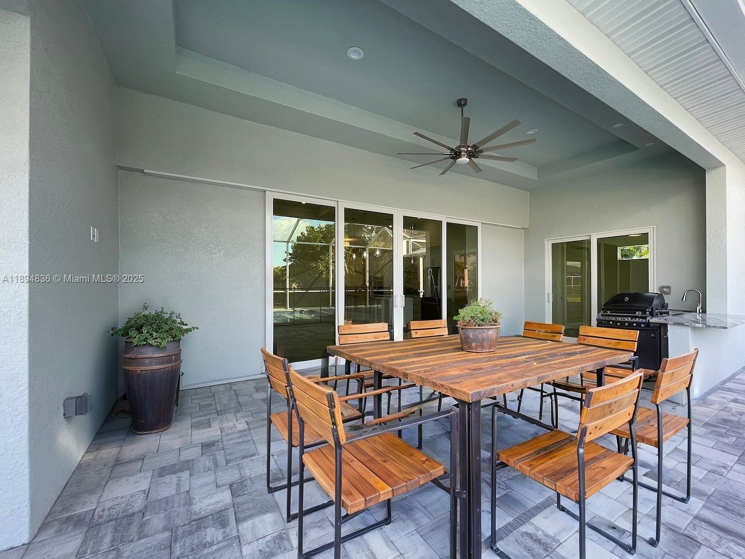 A covered outdoor patio features a wooden dining set, a ceiling fan, and a grill — 2303 SW 43rd Ter, Cape Coral FL 33914, CAPE CORAL, FL