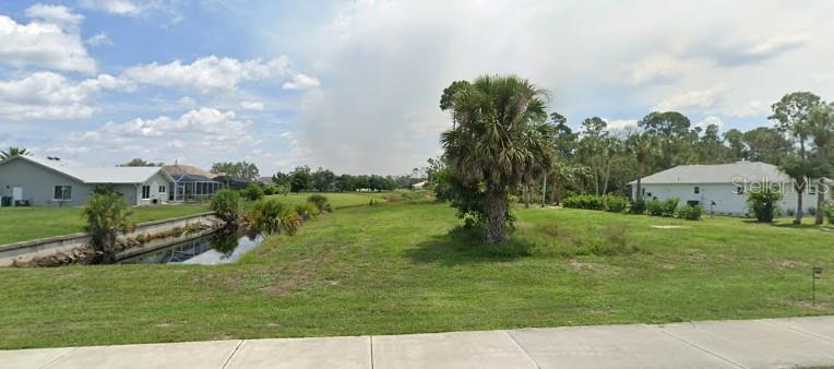 A grassy vacant lot features a small canal and a palm tree near residential houses — 17496 CAPE HORN BOULEVARD, PUNTA GORDA, FL