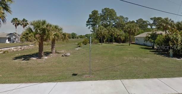 A vacant, grassy residential lot features several palm trees and neighboring houses on both sides — 17496 CAPE HORN BOULEVARD, PUNTA GORDA, FL
