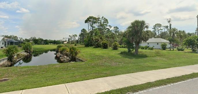 A grassy vacant lot with palm trees, a utility pole, and nearby houses under a sky — 17496 CAPE HORN BOULEVARD, PUNTA GORDA, FL