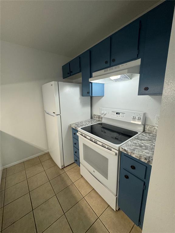 A kitchen features blue cabinets, white appliances, and tan tile flooring — 4000 SW 23RD STREET UNIT 1-106, GAINESVILLE, FL