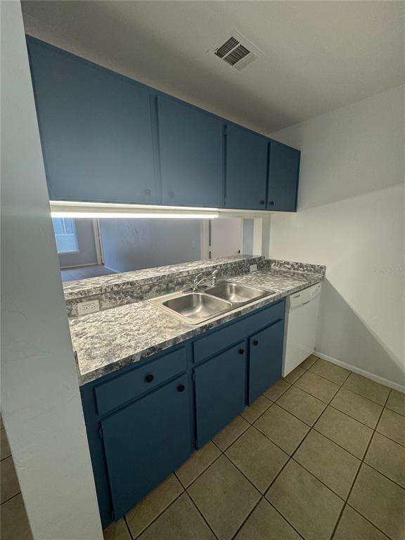 A kitchen features blue cabinets, a gray patterned countertop, a double sink, and tile flooring — 4000 SW 23RD STREET UNIT 1-106, GAINESVILLE, FL