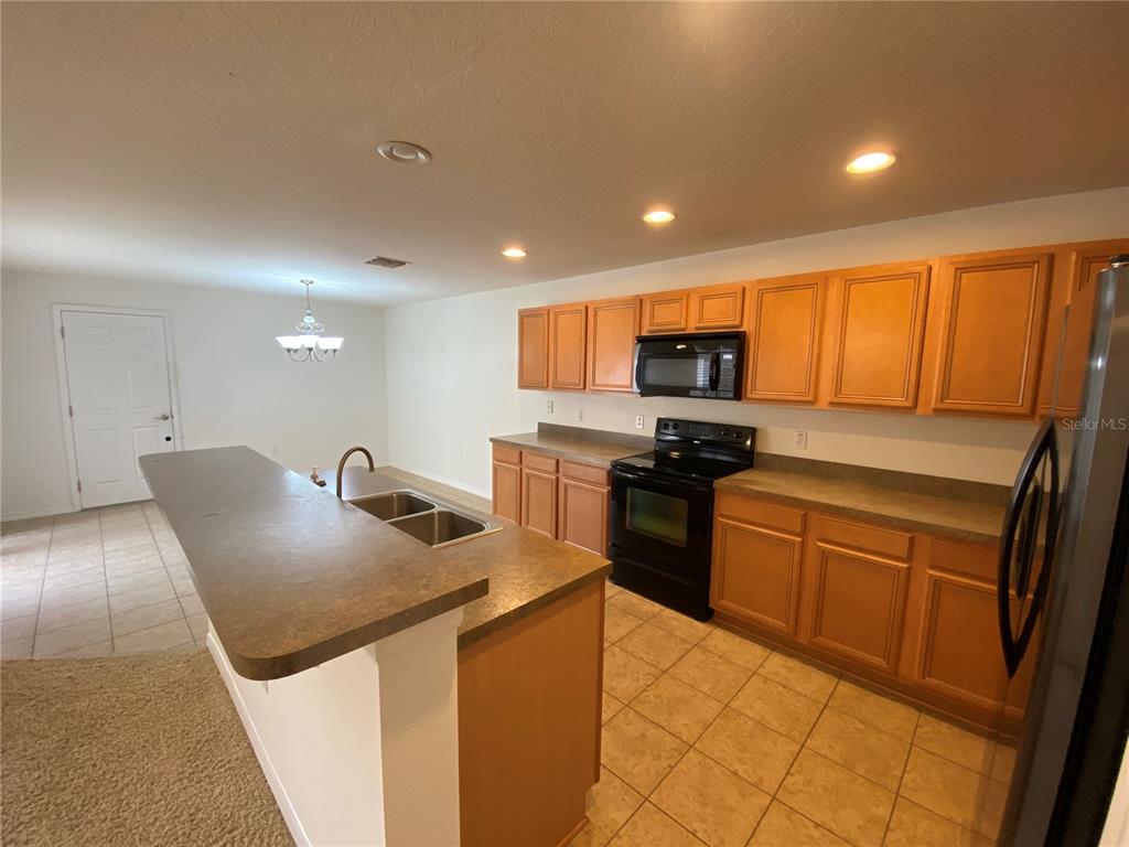 A kitchen features light wood cabinets, dark countertops, black appliances, and tile flooring — 2457 FORMAX DRIVE, ORLANDO, FL