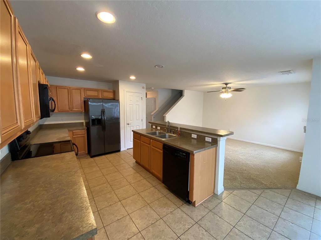 A kitchen with wood cabinets, dark countertops, and tile flooring opens to a carpeted living area — 2457 FORMAX DRIVE, ORLANDO, FL