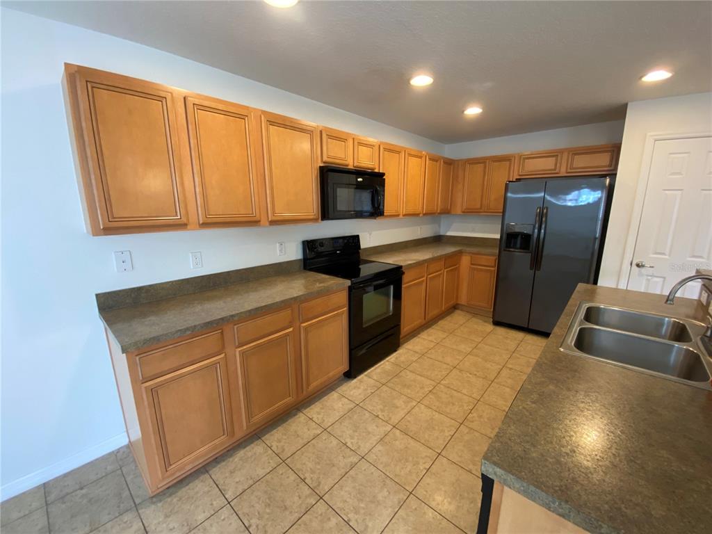 A kitchen features light wood cabinets, dark countertops, black appliances, and tiled flooring — 2457 FORMAX DRIVE, ORLANDO, FL