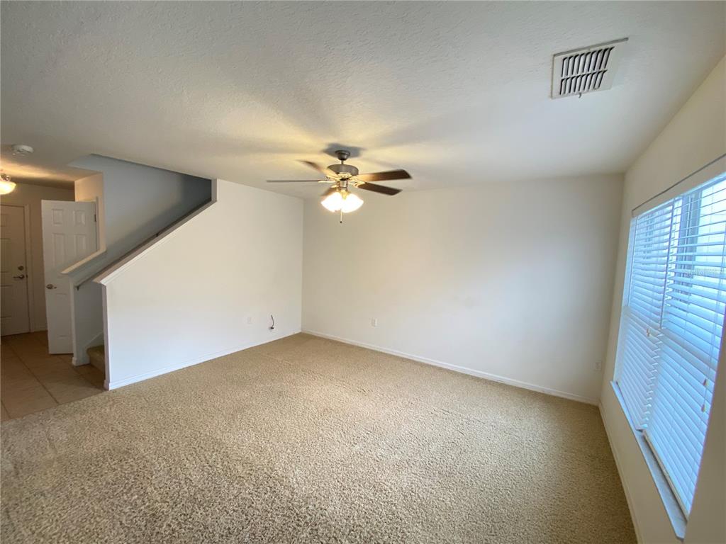 A carpeted living room features a ceiling fan, a staircase, and a large window — 2457 FORMAX DRIVE, ORLANDO, FL