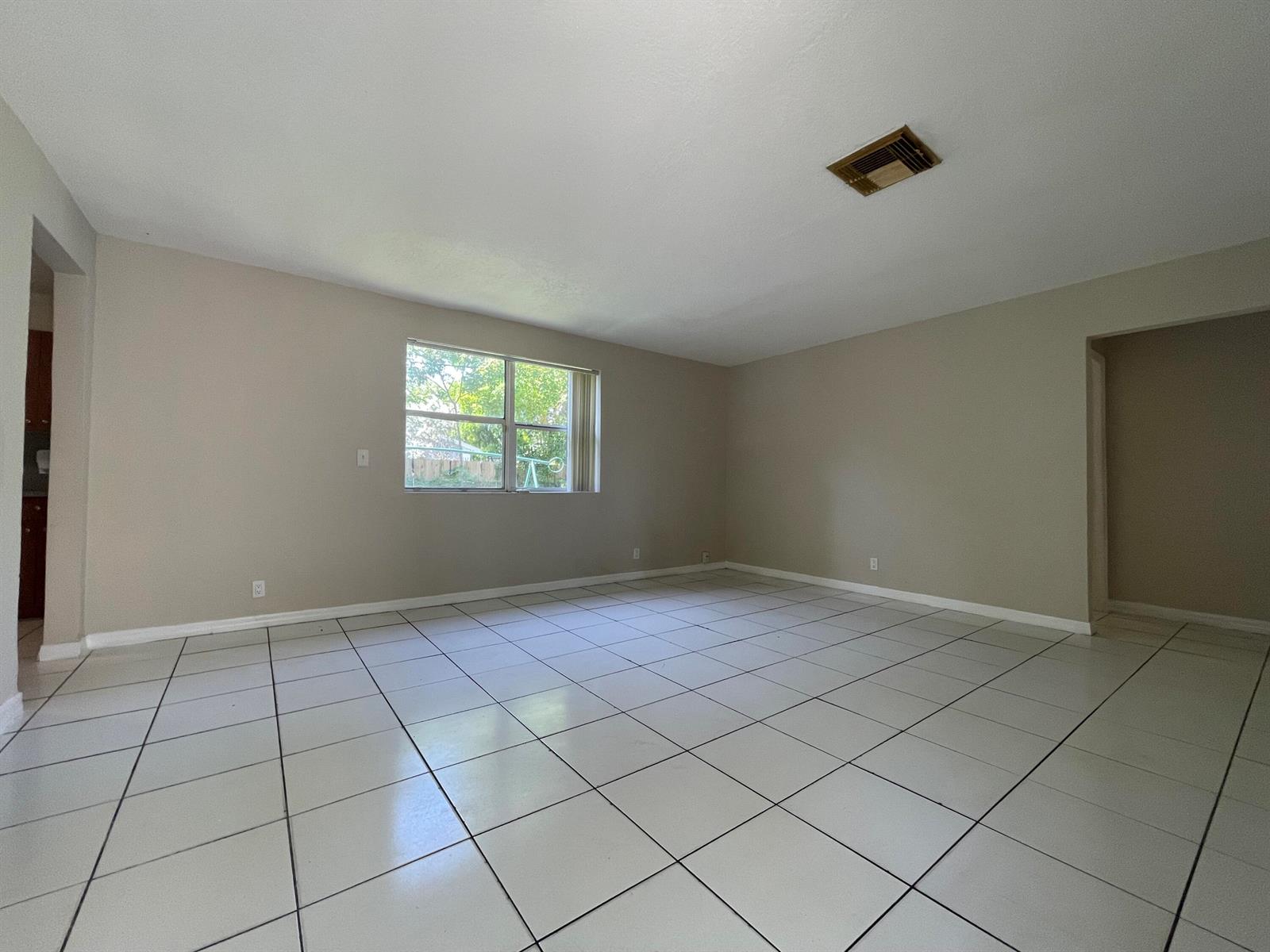 An empty living room features beige walls, white tile flooring, and a single window — 216 NW 12th # 1, Pompano Beach FL 33060, POMPANO BEACH, FL