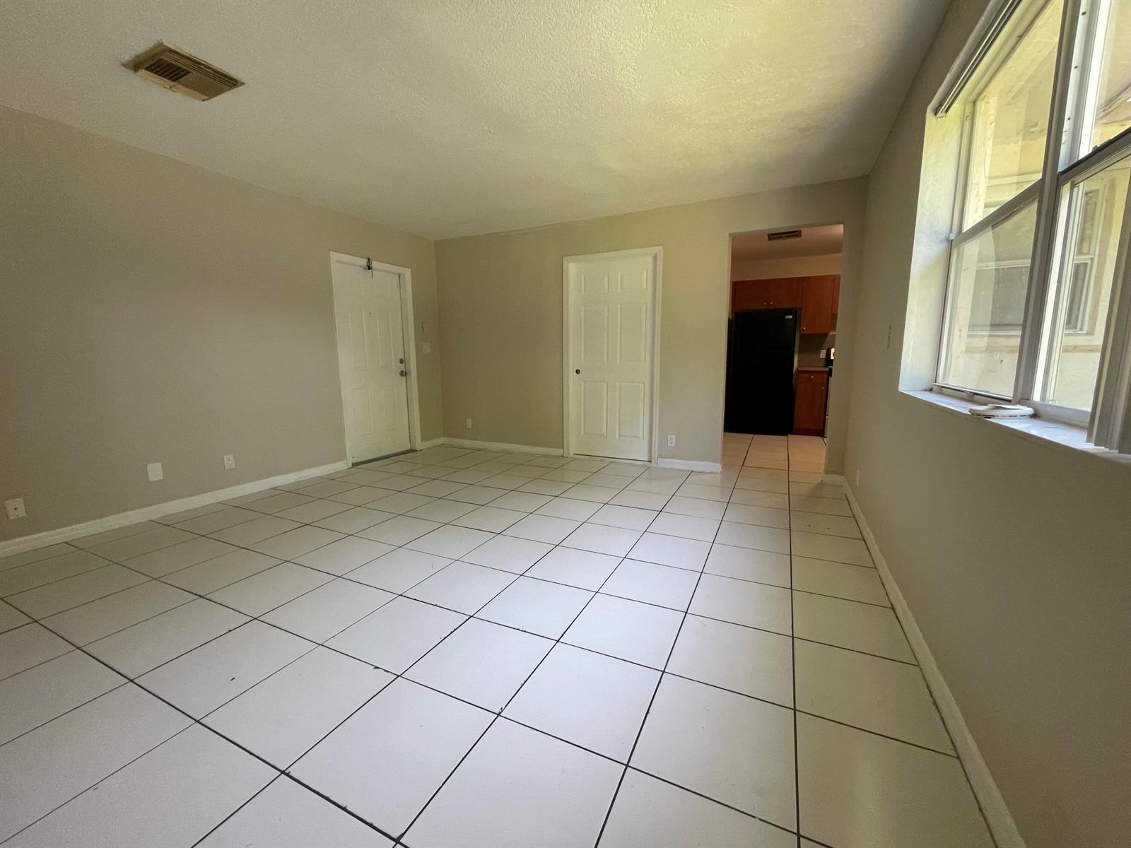 An empty living room features white tile flooring, beige walls, and a doorway to a kitchen — 216 NW 12th # 1, Pompano Beach FL 33060, POMPANO BEACH, FL