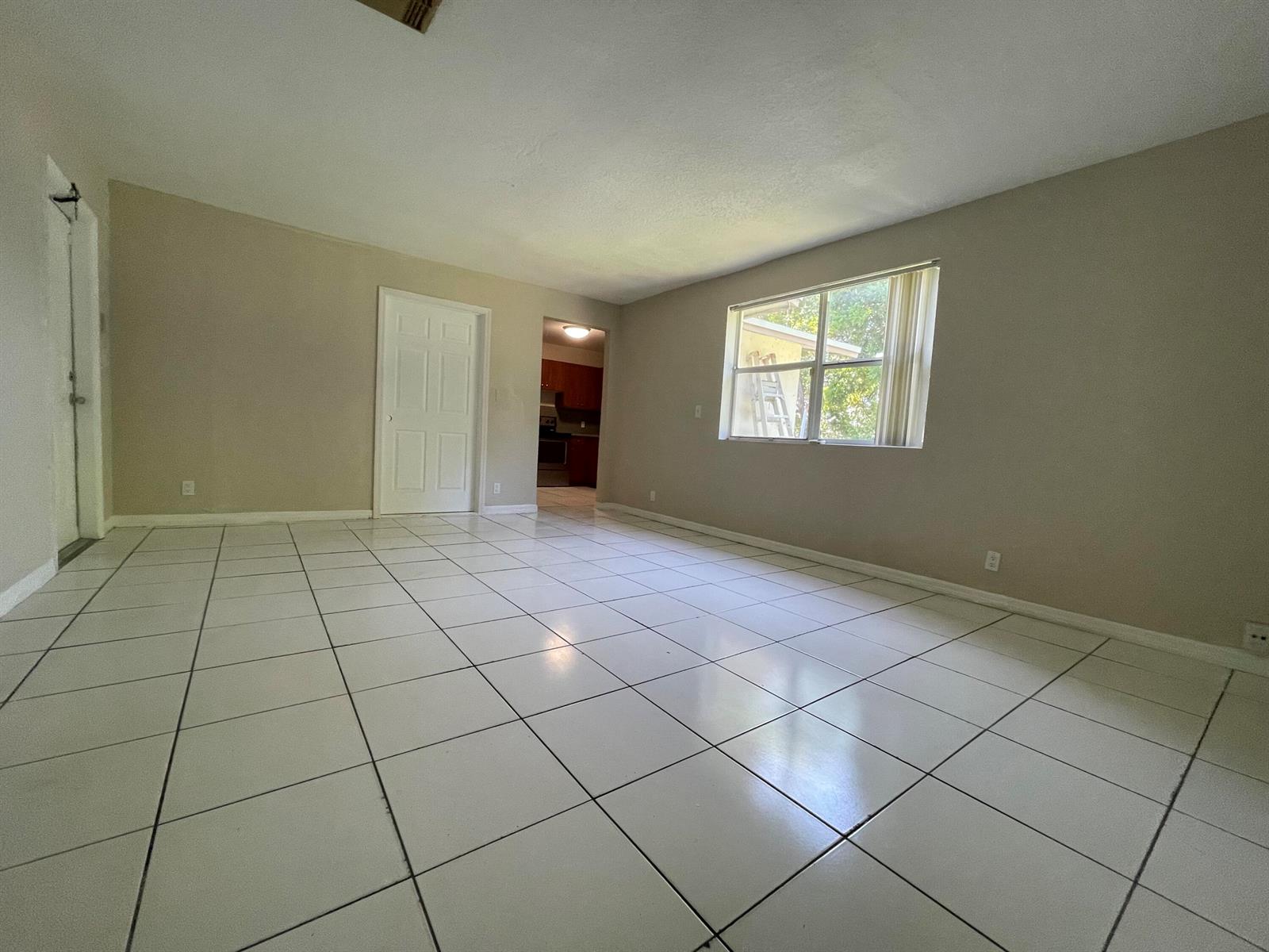 An empty room with white tile flooring, beige walls, a window, and two interior doors — 216 NW 12th # 1, Pompano Beach FL 33060, POMPANO BEACH, FL