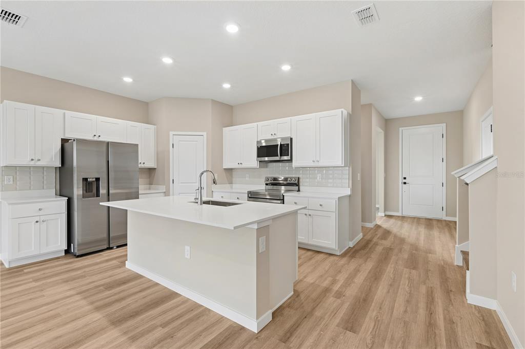 A modern kitchen features white cabinets, stainless steel appliances, a center island, and wood flooring — 4441 NW 37TH STREET ROAD, OCALA, FL